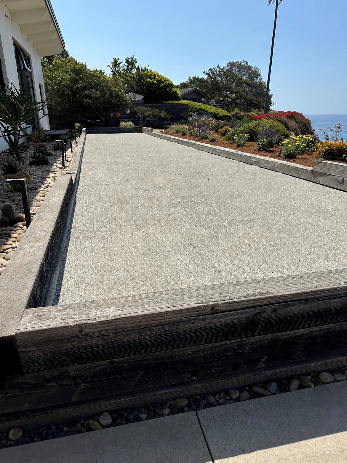 A well groomed oyster shell bocce court sits elevated above floral landscaping and overlooking the ocean in Santa Barbara, California.
